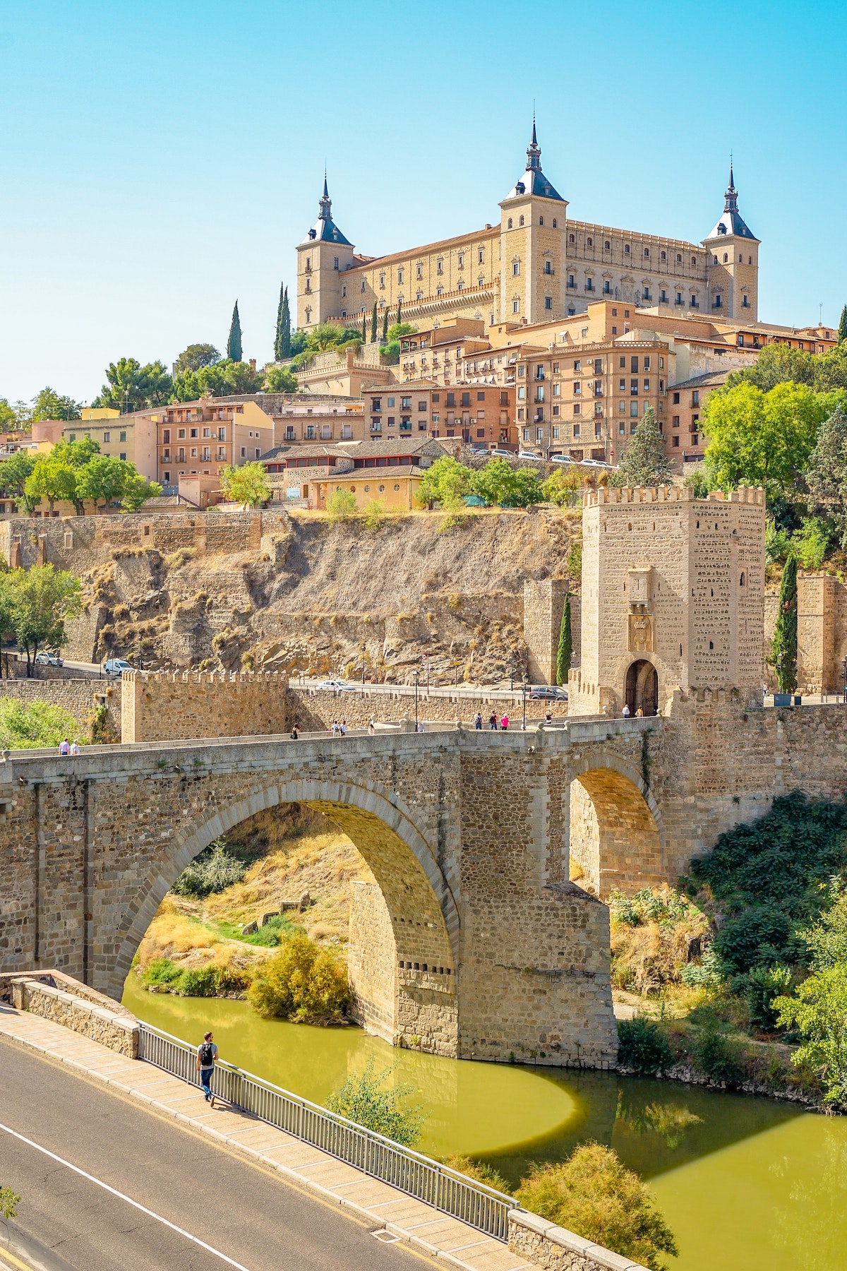 Brown concrete bridge over a river with medieval buildings in background.