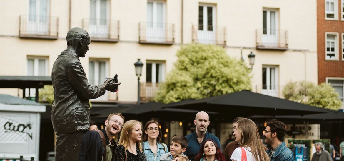 A tour group standing in a plaza in front of a metal statue of a man.