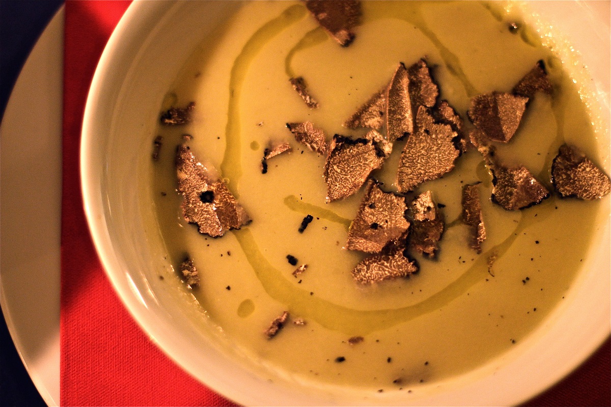 White bowl of yellow soup drizzled with olive oil and shaved truffles