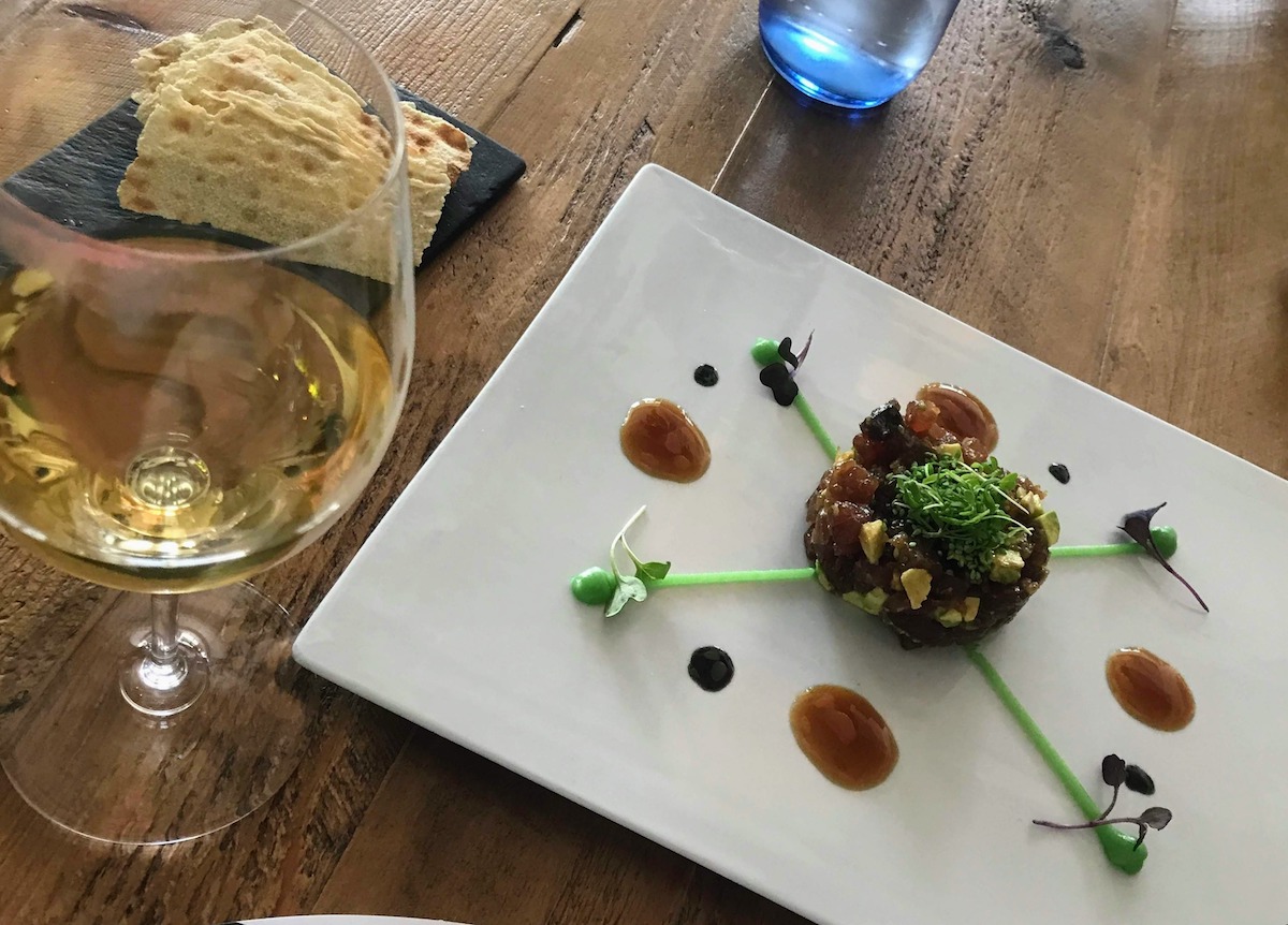 Modern presentation of tuna tartare next to a glass of white wine.