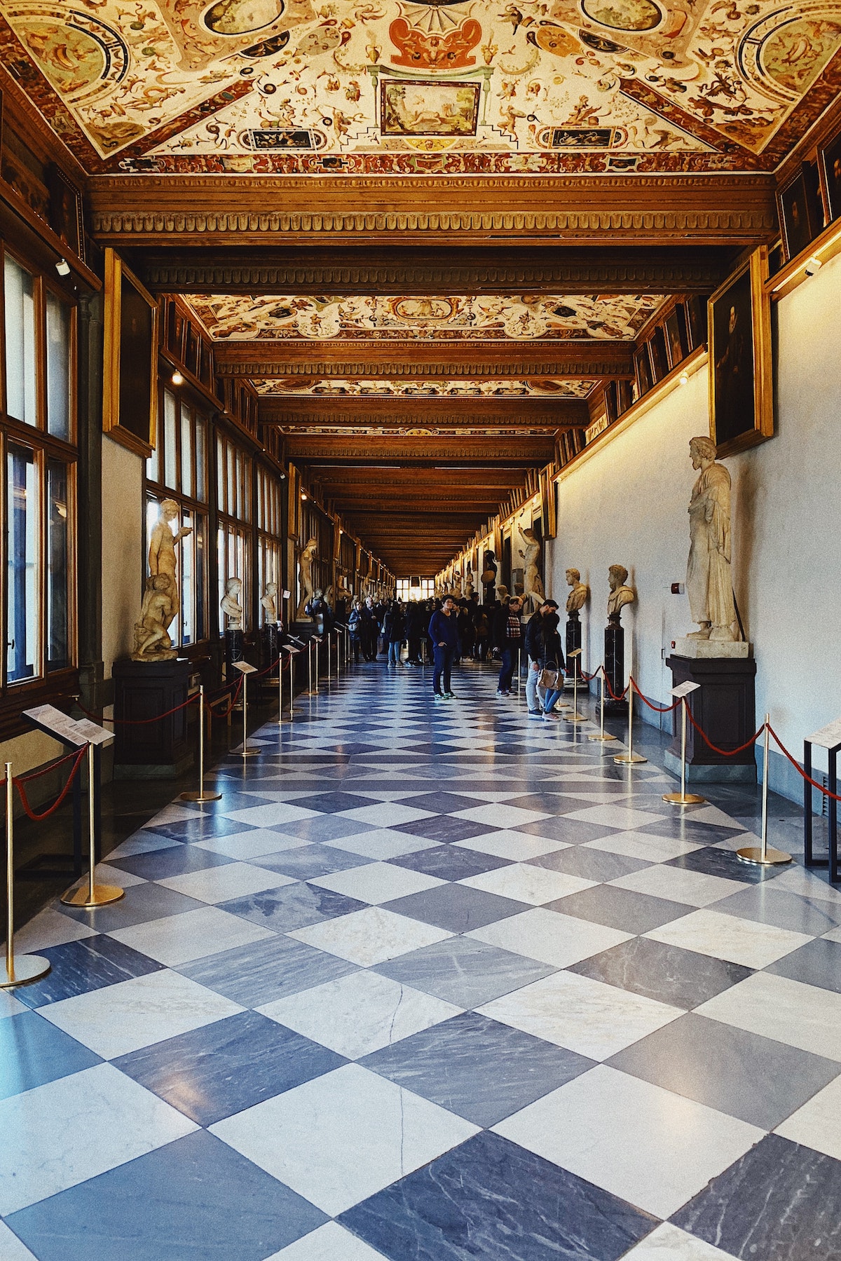 Long hallway of the Uffizi Museum in Florence with black and white checkered floors lined by marble statues