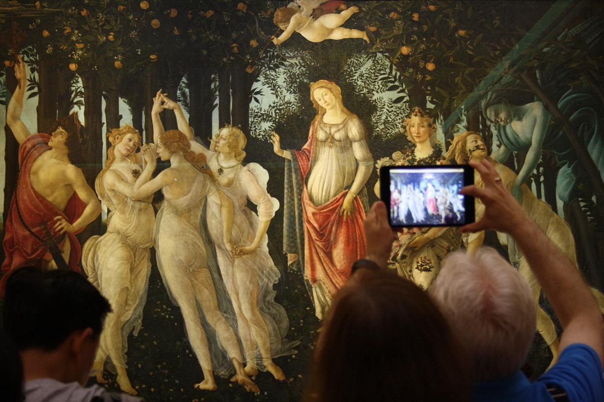 Visitors in an art museum take pictures of a painting of women in a forest