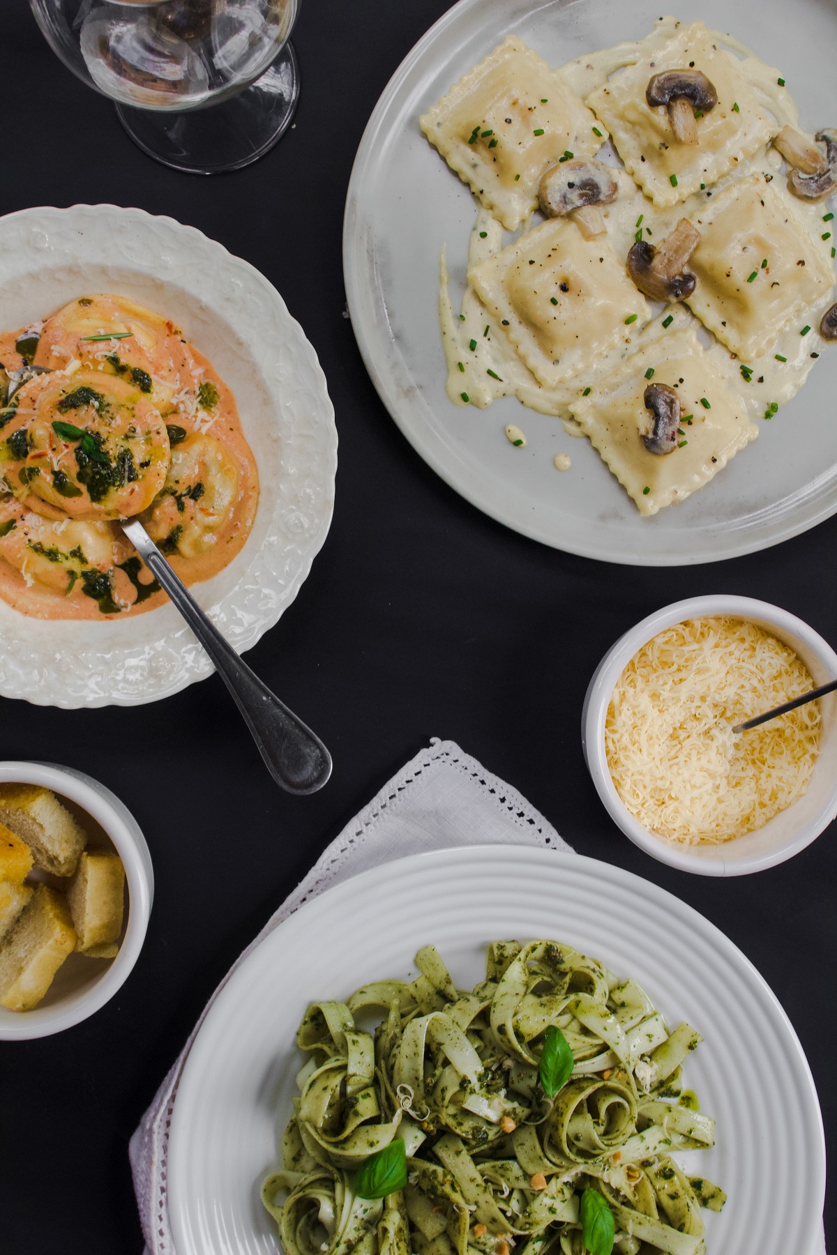 Different pasta dishes - spaghetti, pesto, tortellini - on a restaurant table with cheese.