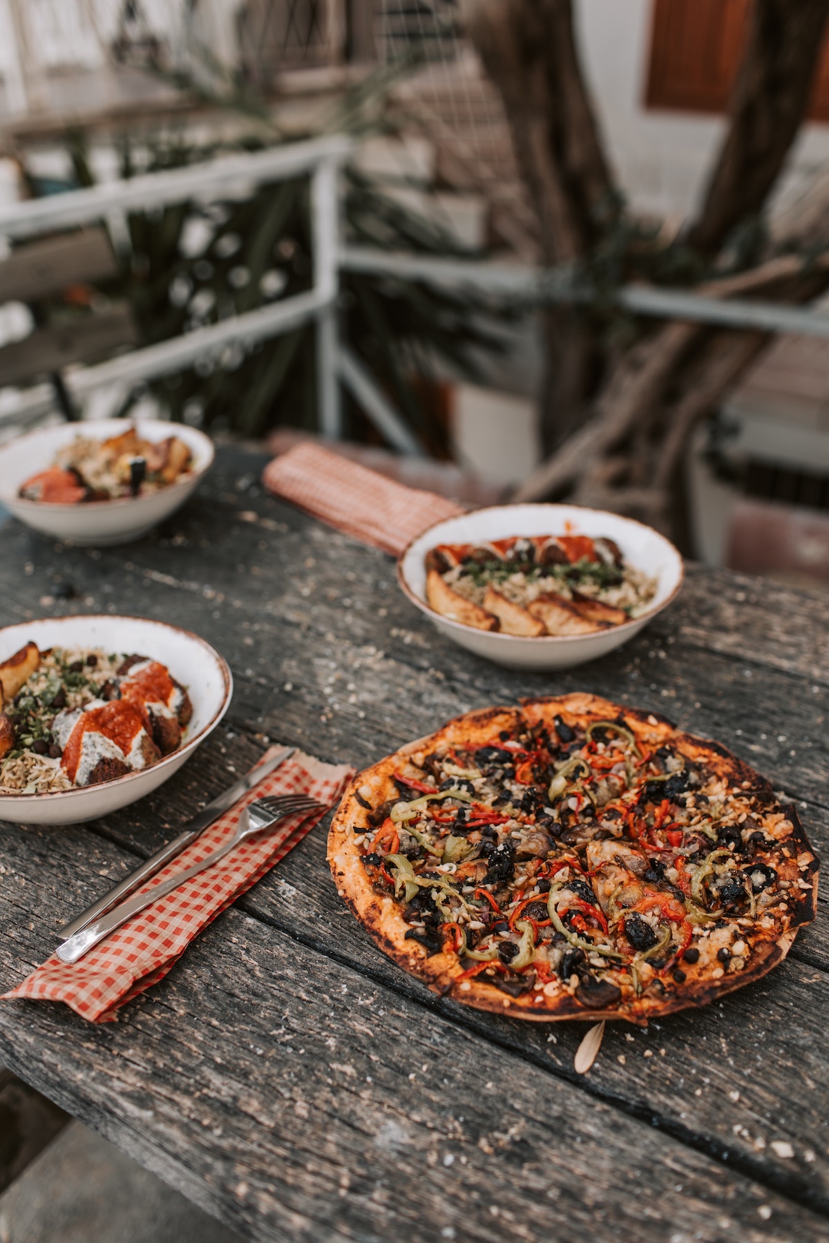 Vegan pizza and bowls of food on a wooden picnic table