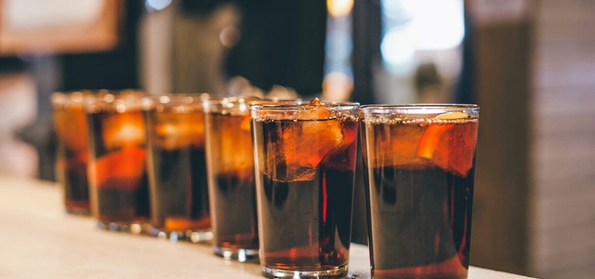 Several small glasses of vermouth lined up atop a bar.