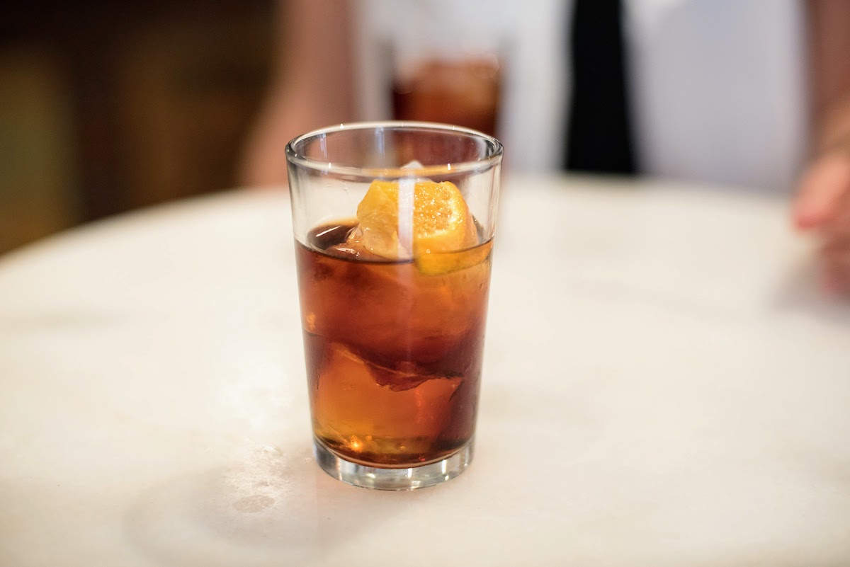 Small glass of red vermouth on the rocks garnished with orange.