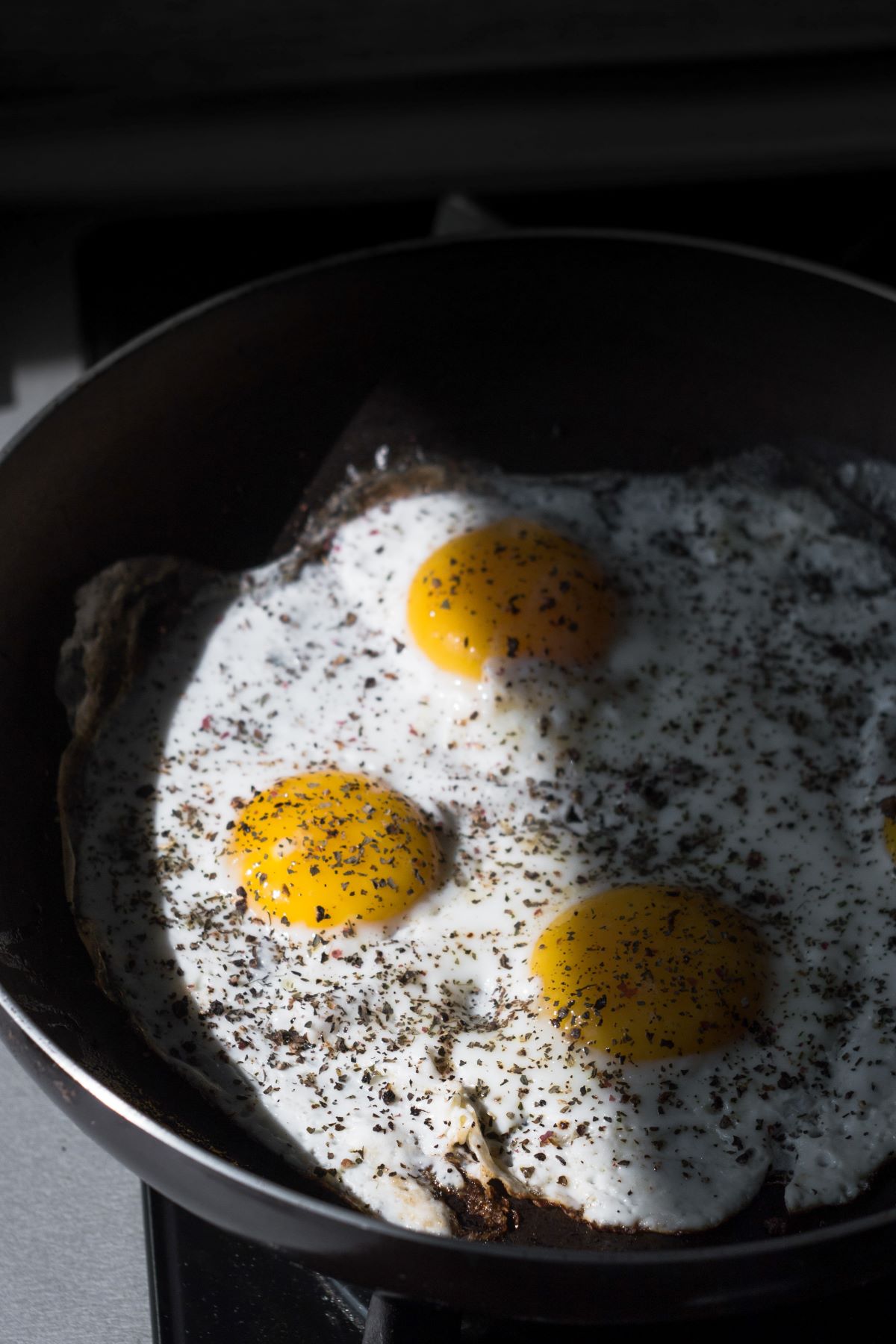 Three eggs being fried in a pan.
