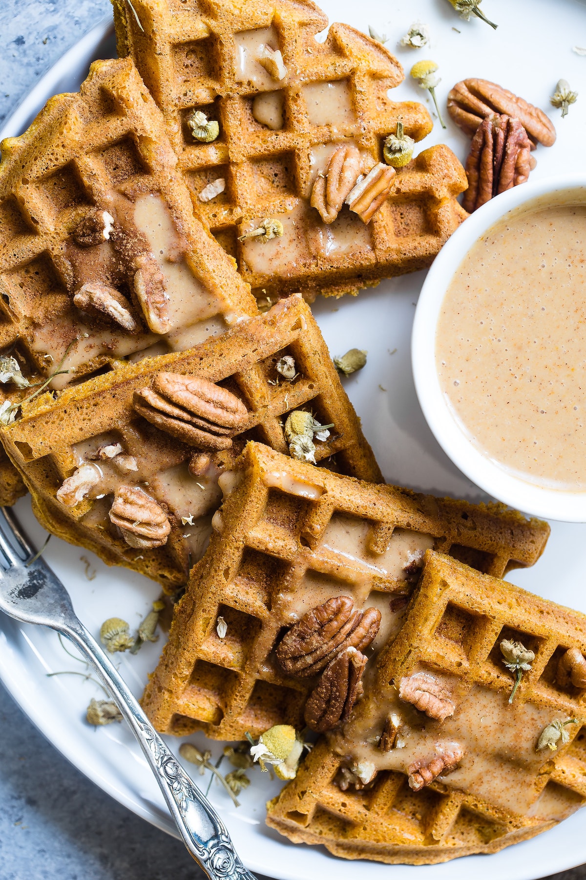 Overhead shot of waffles sprinkled with nuts next to a small cup of light brown sauce.