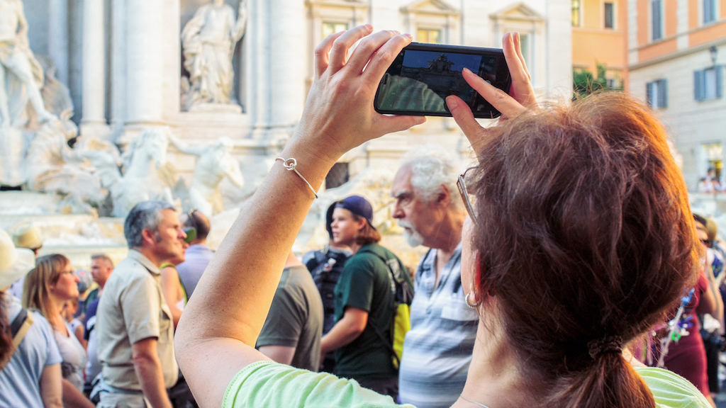 Woman takes a photo with her phone in front of the Trevi Fountain in Rome