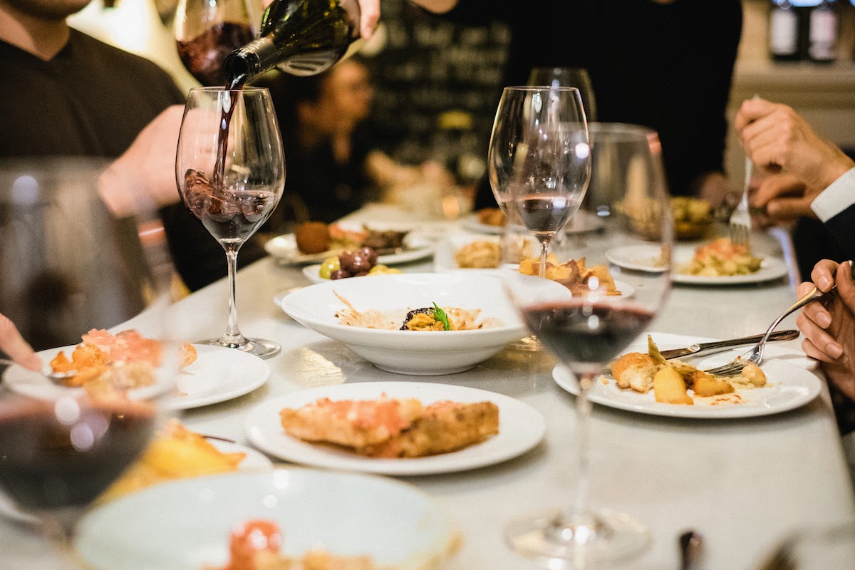 Three glasses of red wine on a table among several small tapas-style dishes.