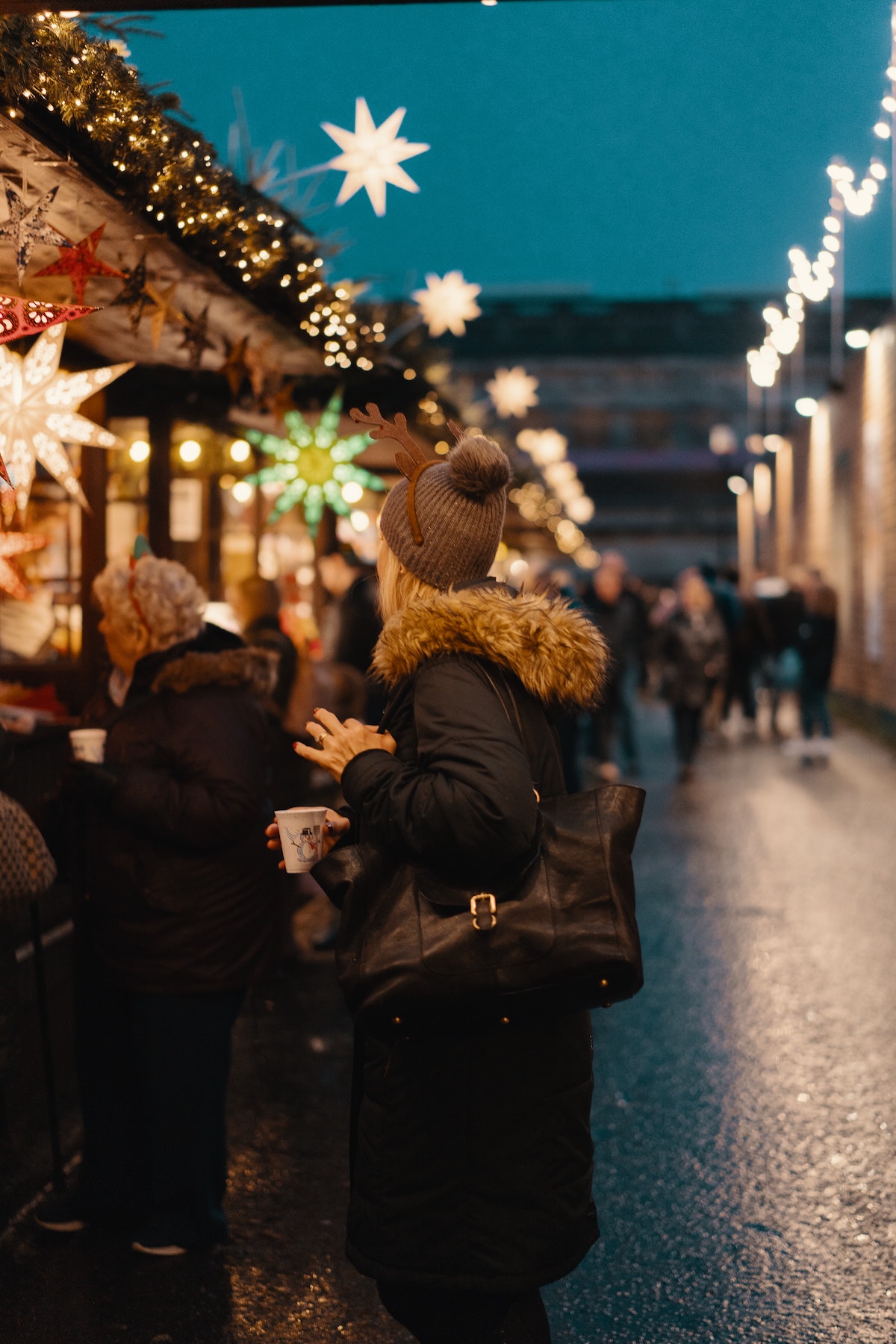 Woman browsing the stalls at a brightly lit Christmas market.