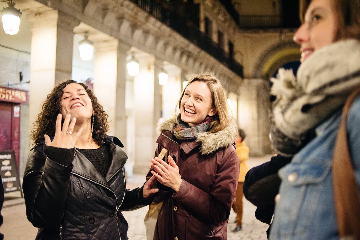 Three women talking and laughing in a brightly lit plaza.