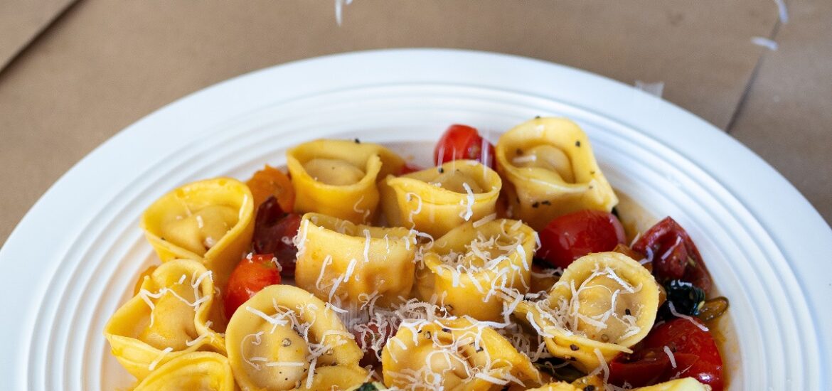 Plate of tortellini with tomatoes and herbs with fresh cheese grated on top