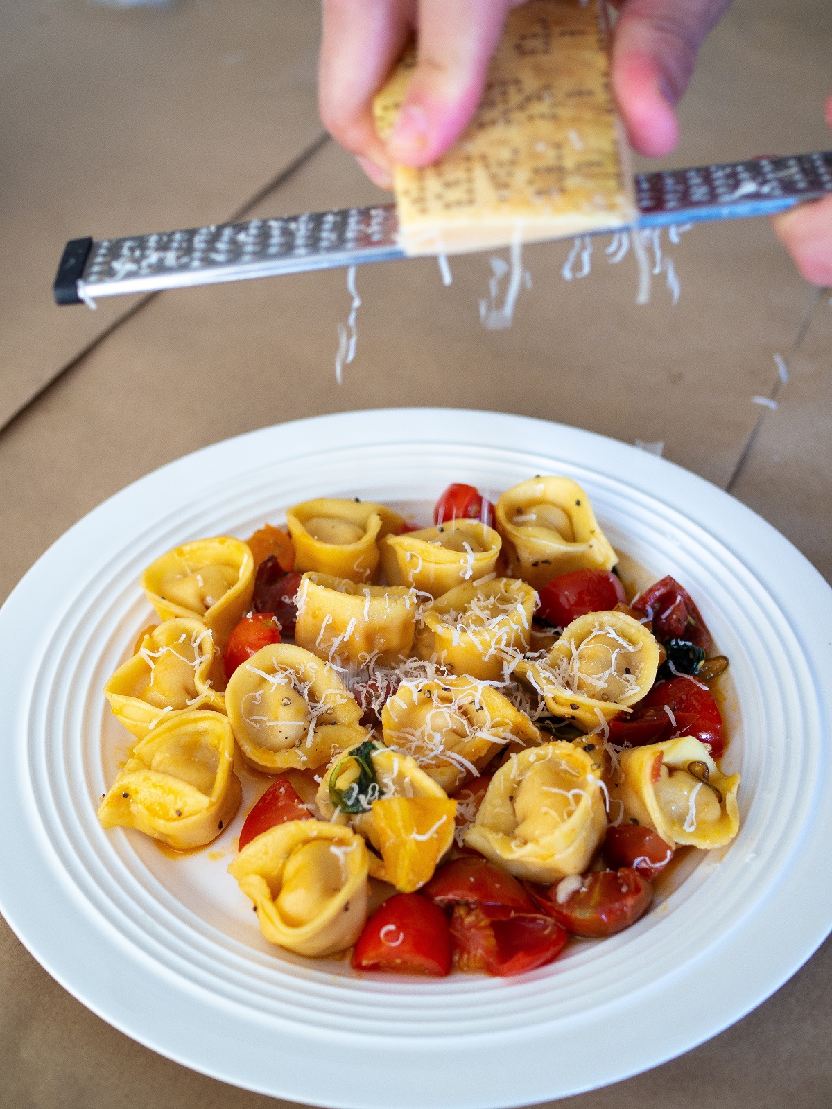 Plate of tortellini with tomatoes and herbs with fresh cheese grated on top